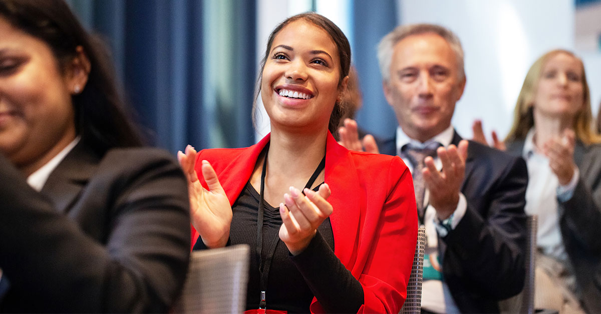 A smiling woman clapping as part of a diverse conference audience   A smiling woman clapping as part of a diverse conference audience