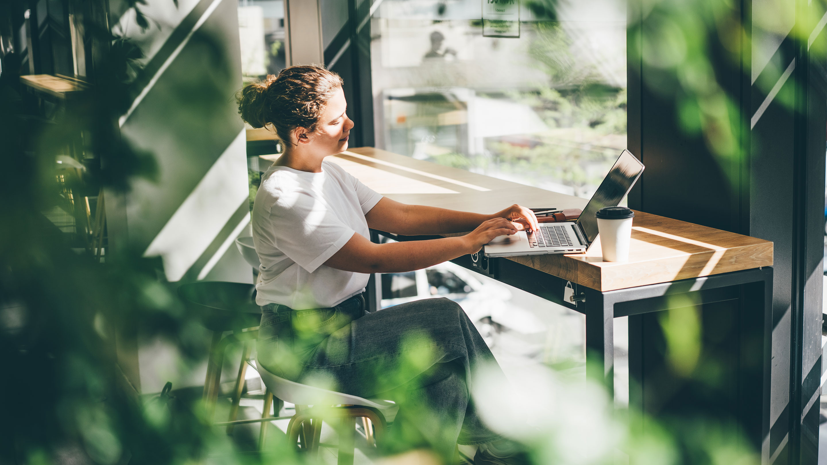 Woman sat working on a laptop surrounded by houseplants 