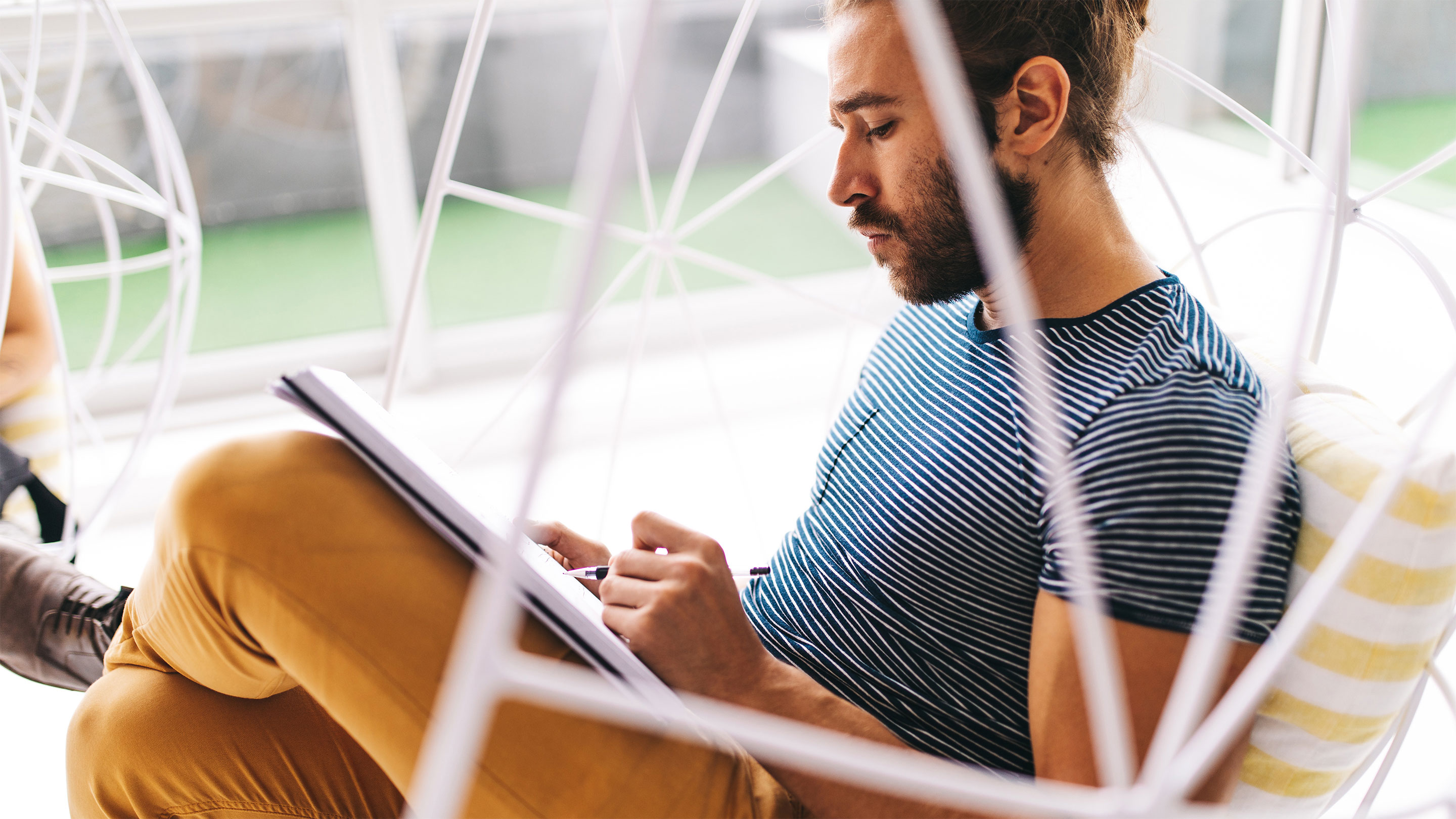 Man sat in a hanging chair writing on a notepad Man sat in a hanging chair writing on a notepad