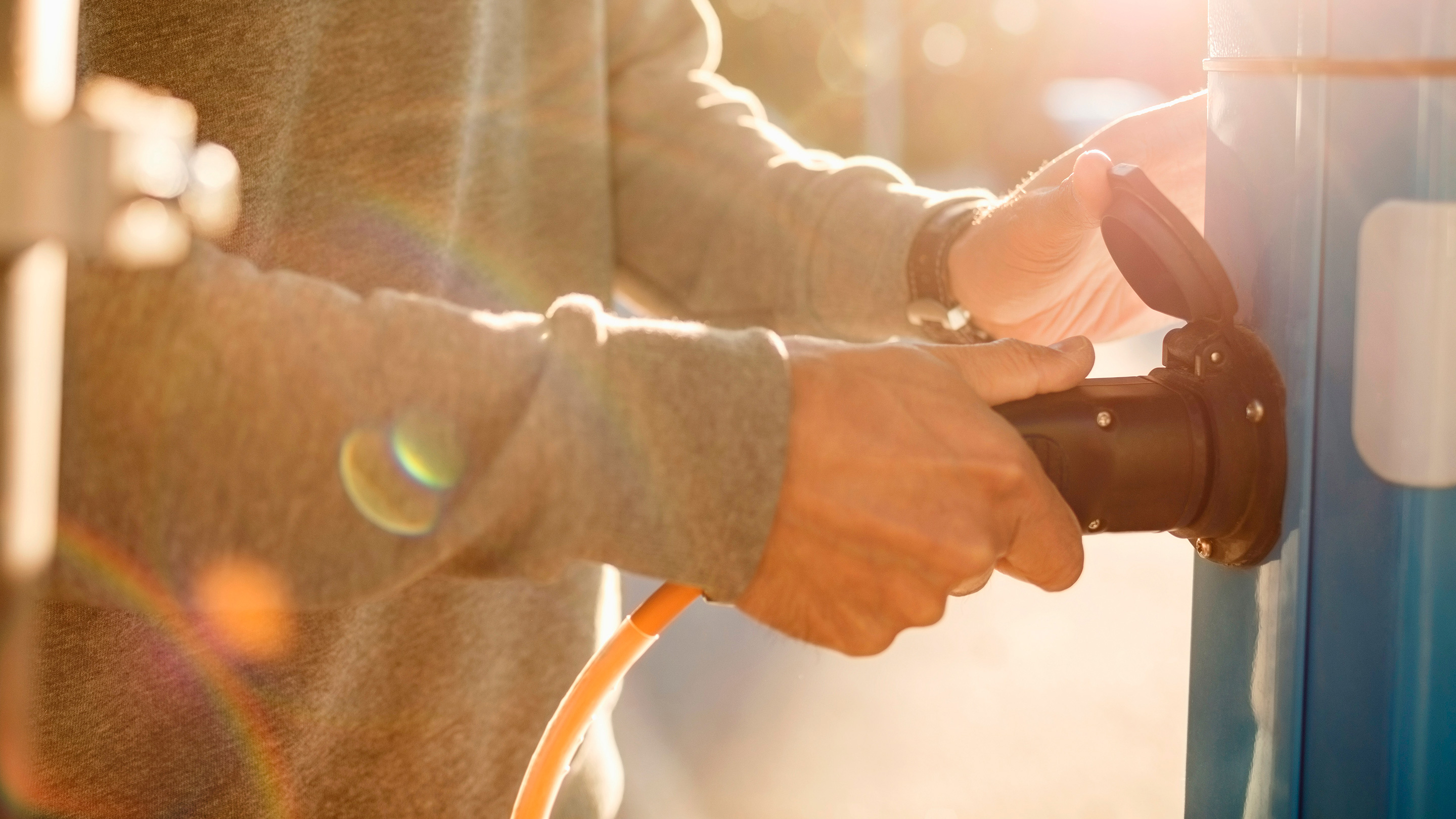 Man wearing grey sweatshirt plugging in a charger at an electric charging point Man wearing grey sweatshirt plugging in a charger at an electric charging point