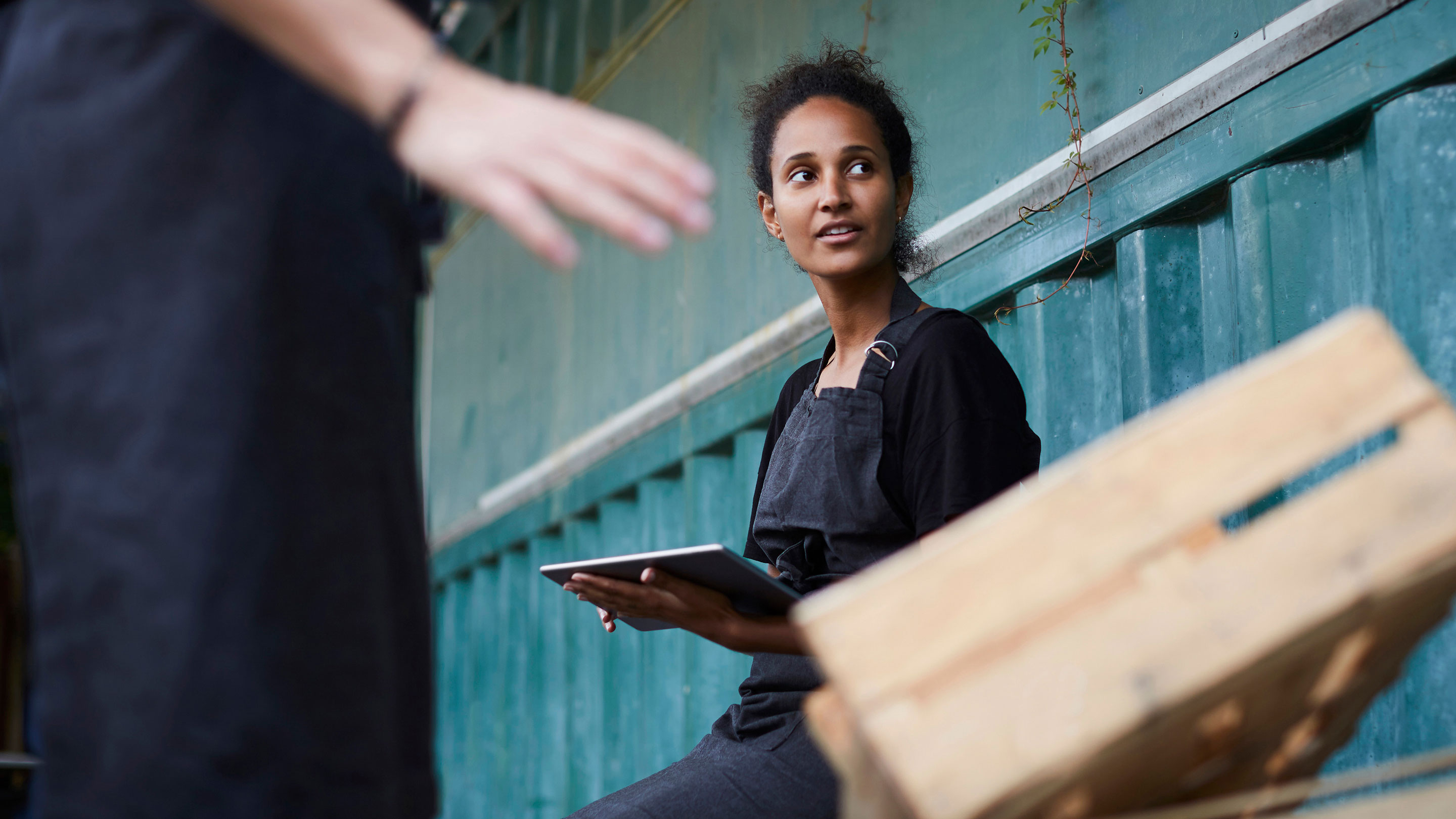 Woman with a clipboard sitting by a shipping container alongside empty wooden pallets  