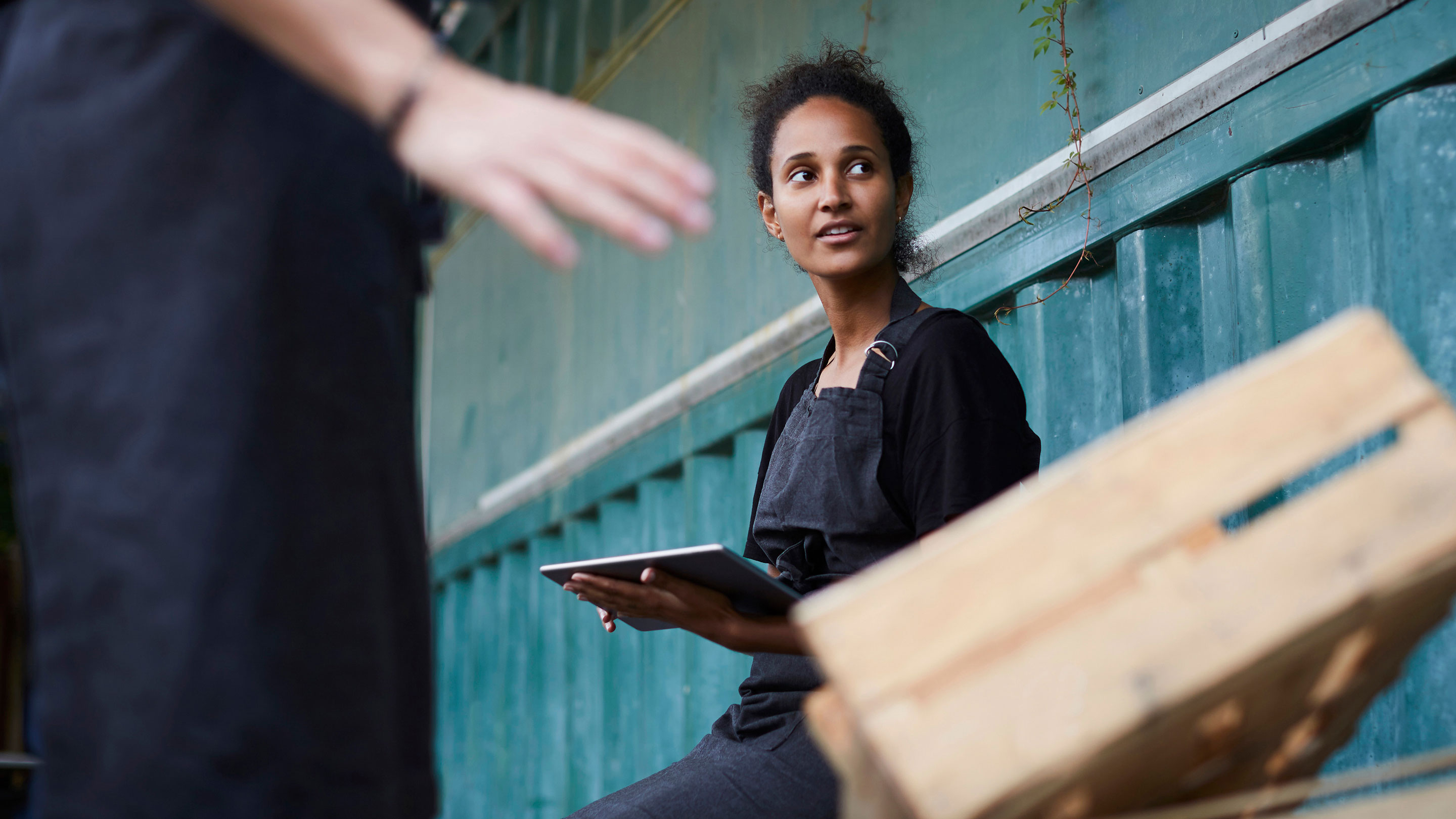 Woman with a clipboard sitting by a shipping container alongside empty wooden pallets Woman with a clipboard sitting by a shipping container alongside empty wooden pallets