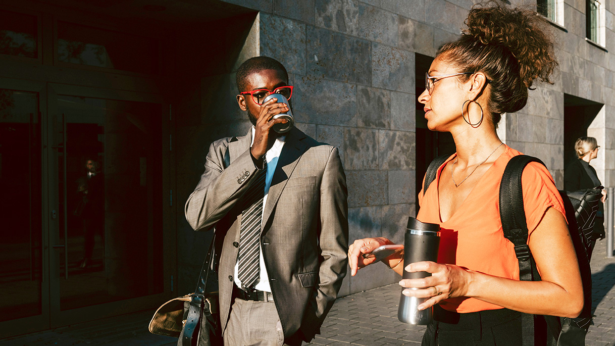 Smartly dressed man walking and talking to his female colleague whilst both are drinking coffees  Smartly dressed man walking and talking to his female colleague whilst both are drinking coffees